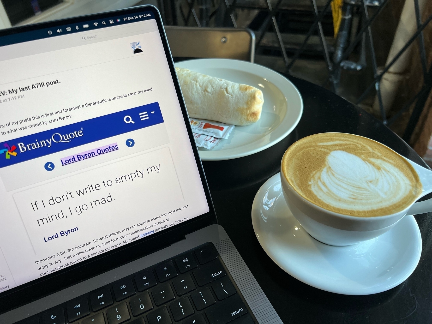 a latte, a breakfast burrito, and a partial view of a laptop. 