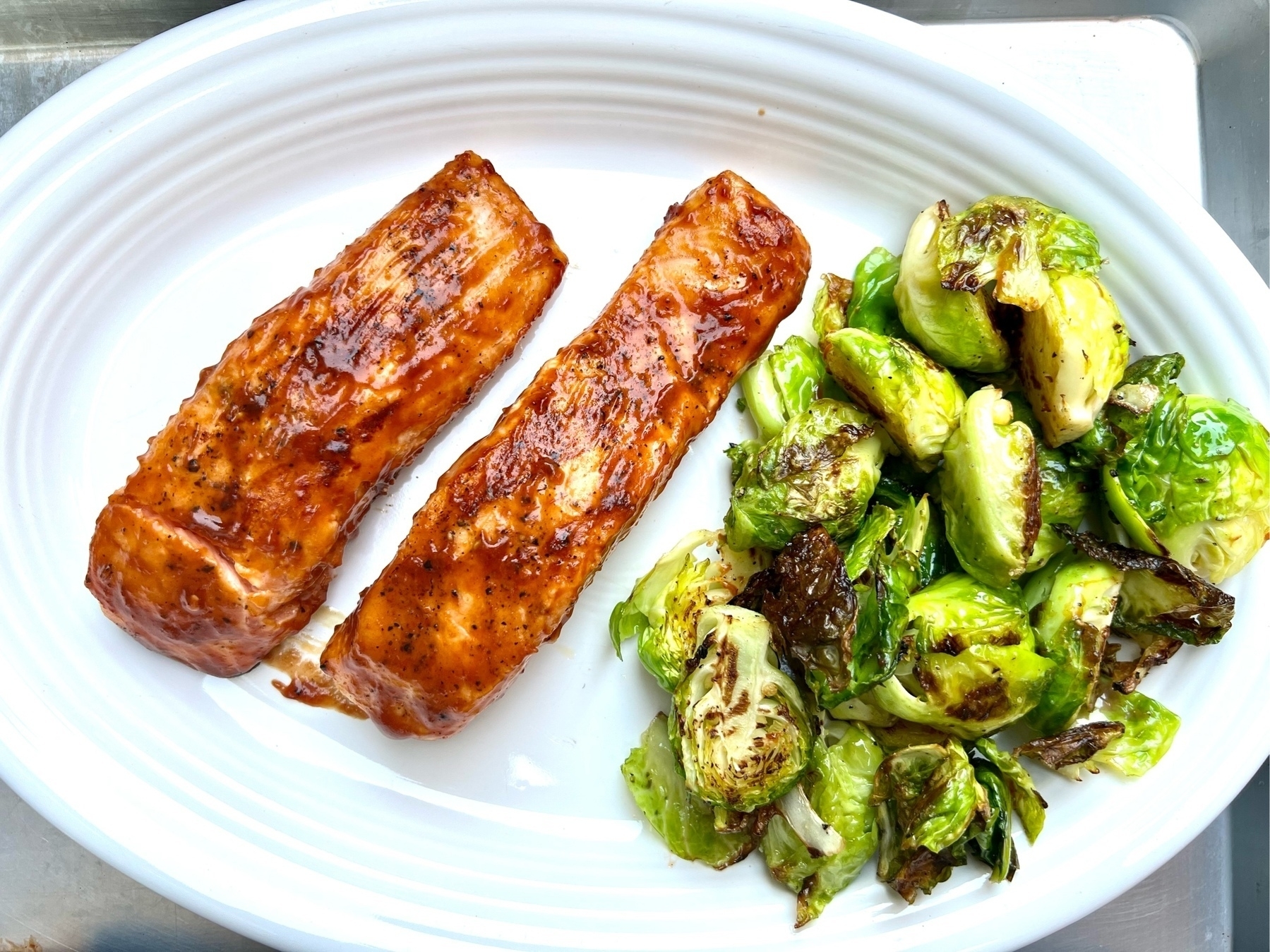 bbq grilled salmon filets kn a white oval plate. they are accompanied by grilled brussel sprouts. 