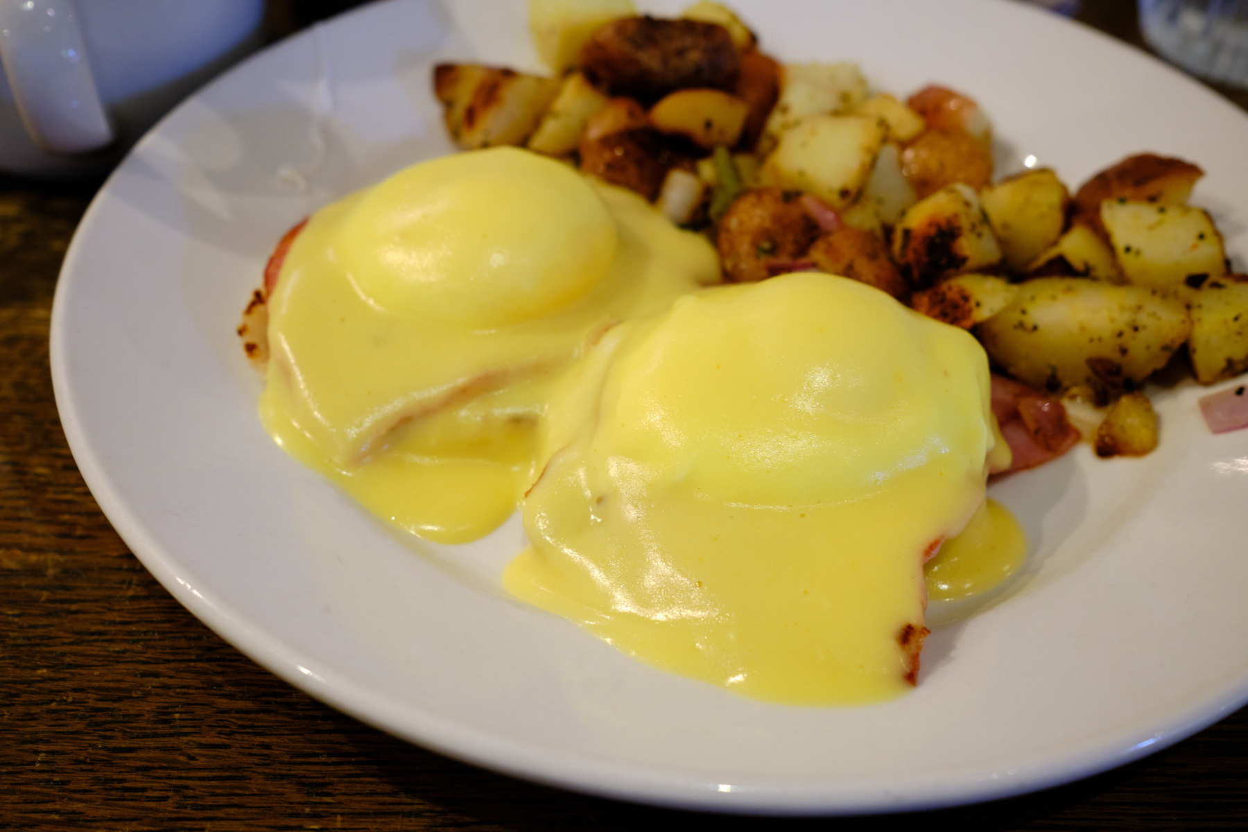 a plate of eggs Benedict with extra hollandaise sauce and a side of breakfast potatoes.