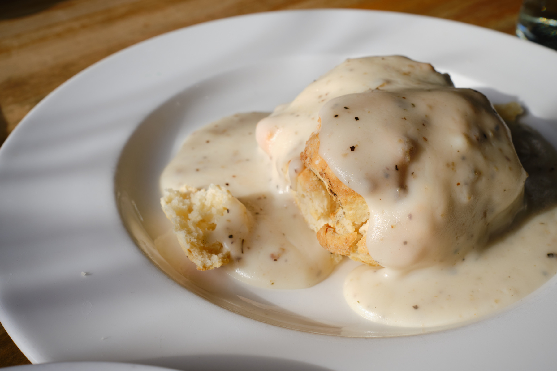 a single biscuit, covered in sausage gravy, lit by morning sunlight coming through a window. 